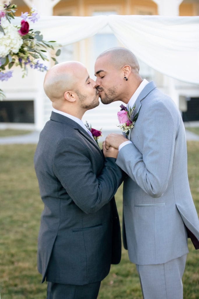 Gay couple kissing under their arbor after being pronounced

