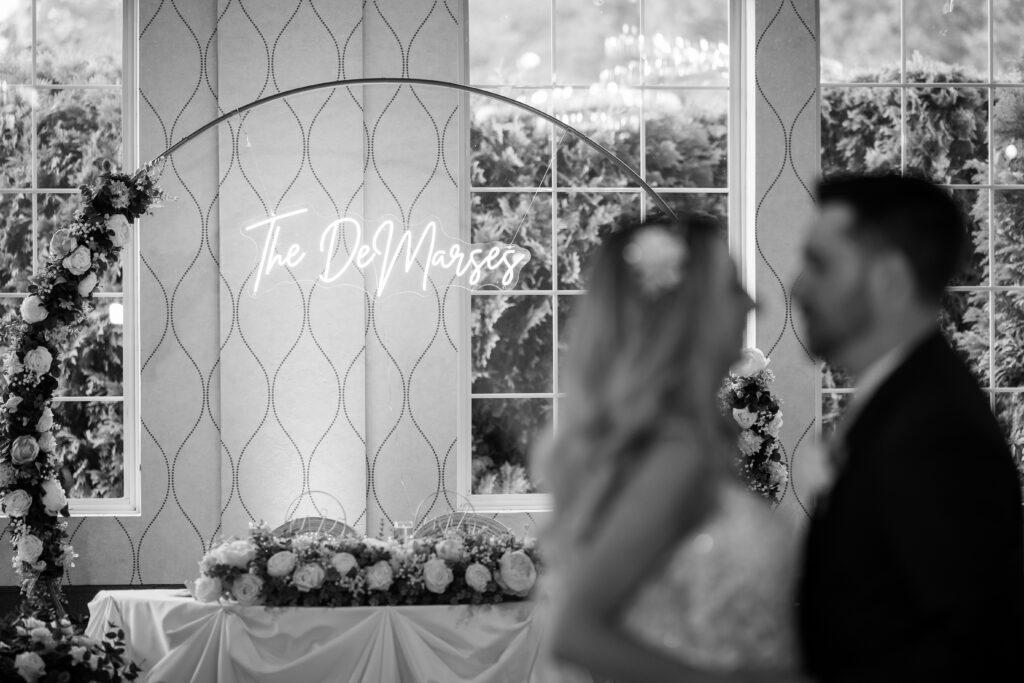 "The DeMarcos" neon light during the couples first dance. Bride and groom are blurred in the forefront